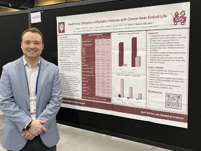 male student smiling and standing by research poster